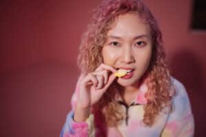 A woman bites into a gummy candy against a pink background.