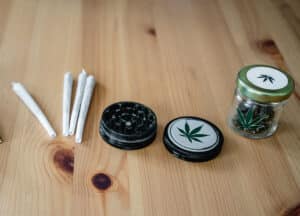Storing marijuana buds in a small glass jar, accompanied by a grinder and several rolled joints, creates a relaxed, herbal atmosphere