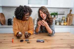 Two cheerful multi-ethnic female friends are preparing a joint of legal marijuana in a domestic kitchen